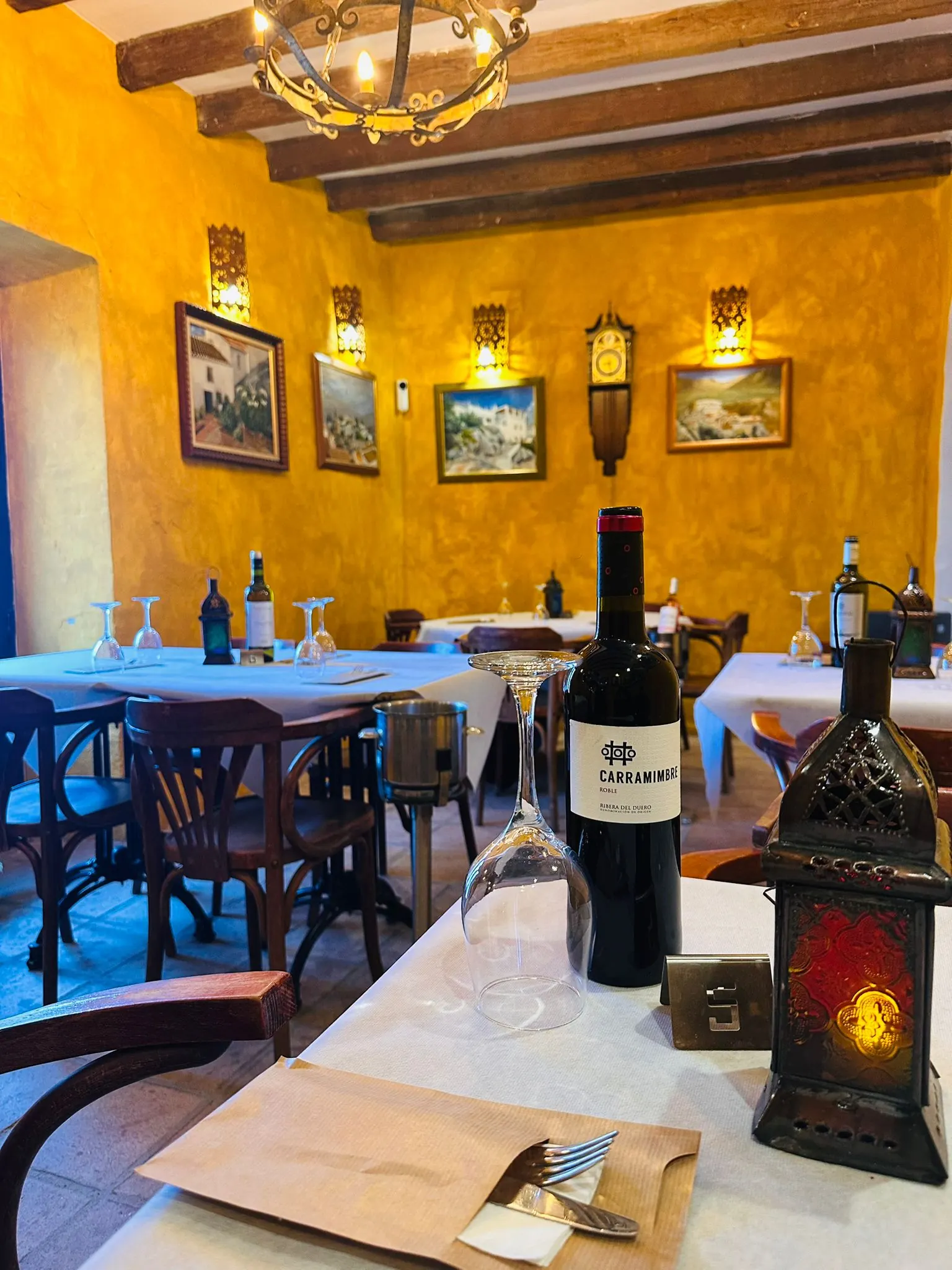 Mesa puesta en el salón ocre, con una botella de vino y un farol
