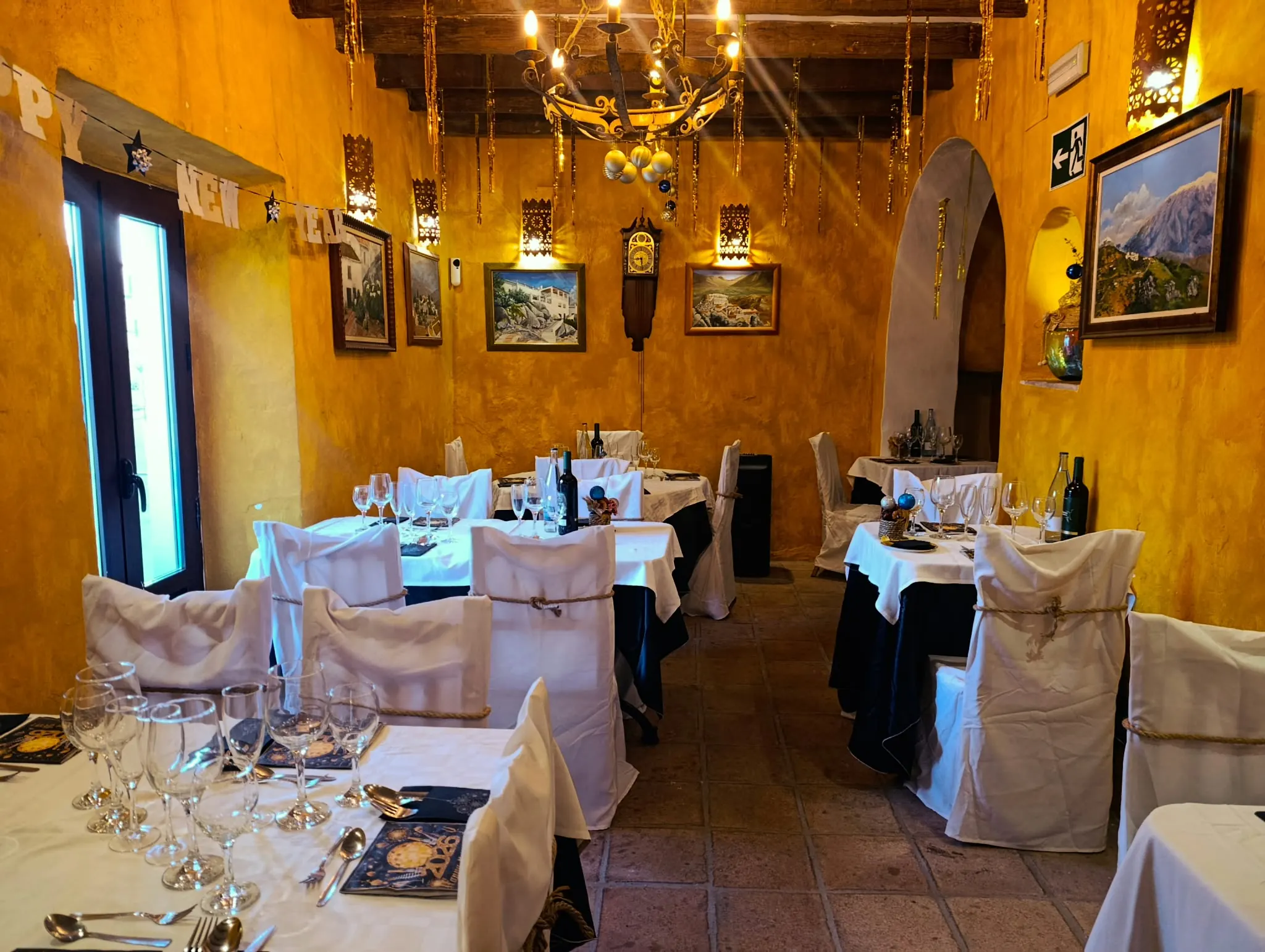 Salón de paredes ocre con vigas de madera, lámpara de hierro y mesas vestidas