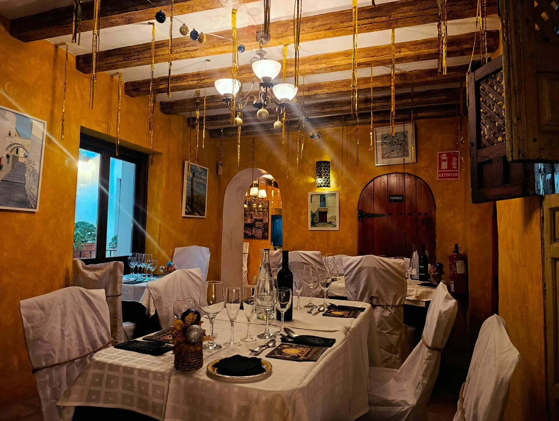 Salón ocre con puerta de madera en arco, ventana y mesas montadas